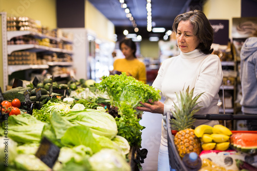 Female elderly shopper choosing ripe salad at grocery supermarket © JackF
