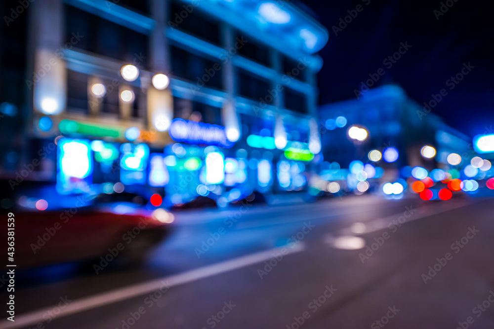 Nights lights of the big city, cars go down the avenue past the bright shop windows. Wide-angle view, defocused image