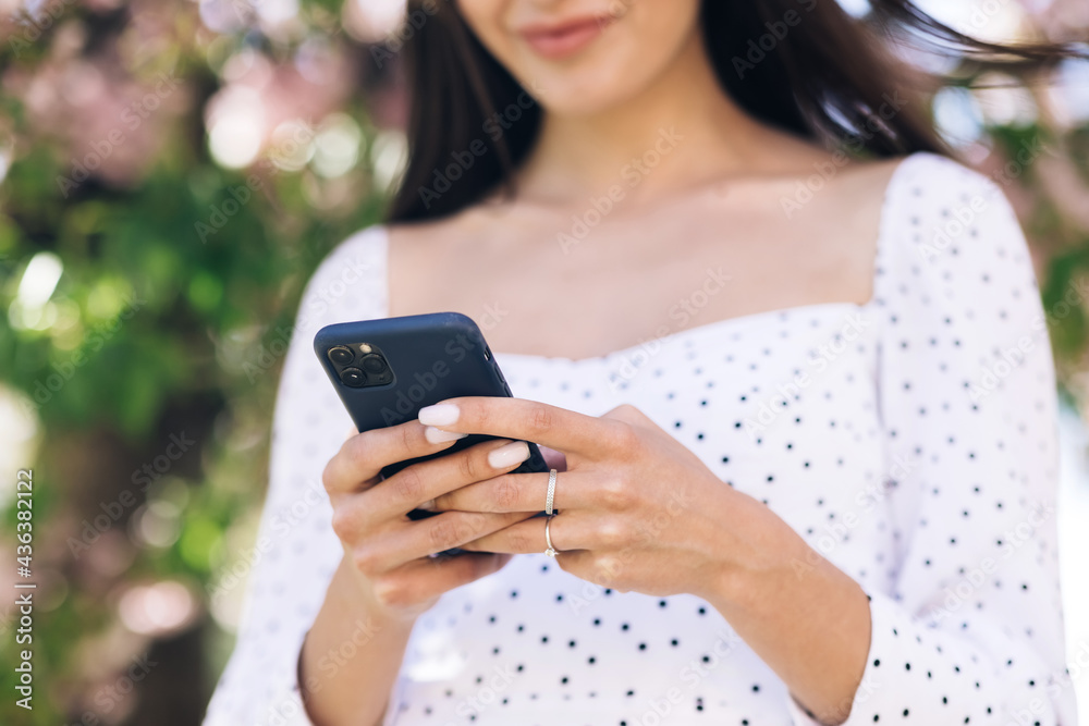 Woman wearing white dress using smartphone. Girl using social media application text messages receive news smiling outdoor. Communication, social networks, online shopping concept. Technology Woman wearing white dress using smartphone. Girl using social media application text messages receive news smiling outdoor. Communication, social networks, online shopping concept. Technology