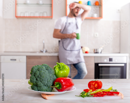 Tired young man blurry standing behind fresh vegetables broccoli peppers.