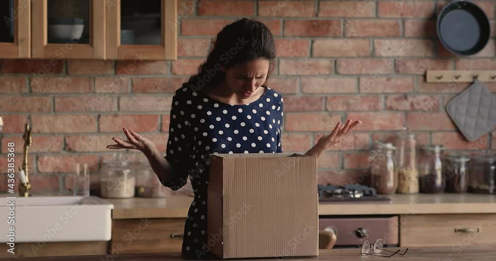 Confused young hispanic woman unwrapping cardboard box, feeling disappointed with received wrong or damaged item, displeased with negative online shopping experience or unreliable delivery service.