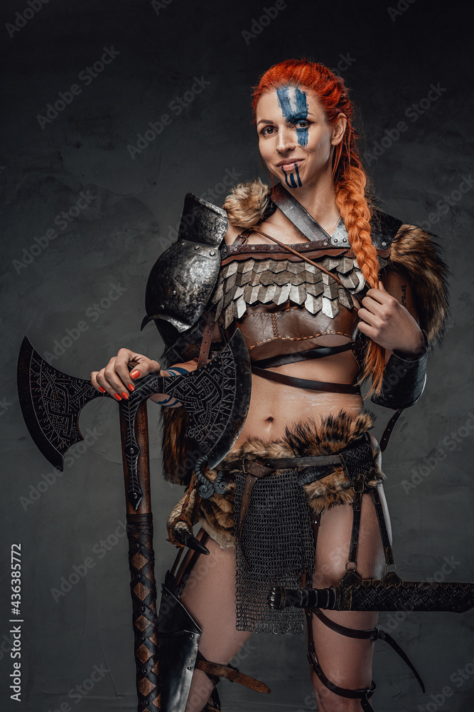 Obraz premium Serious nordic female warrior with axe and armour in dark background