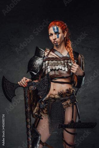 Serious nordic female warrior with axe and armour in dark background © Fxquadro