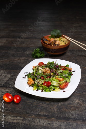 salad with shrimp and herbs and a plate with ramen on a wooden background