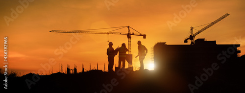Silhouette engineer construction work control and tower crane background on natural sunset sky.,Heavy industry and building construction work concept in banner photo