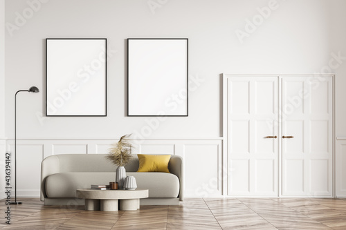 Living room design interior. Modern stylish home area. Two framed mock up posters on white wall. Wooden parquet floor. Beige couch under the placards.