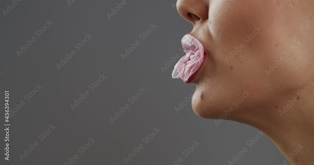 Young woman popping bubble gum on grey background, closeup