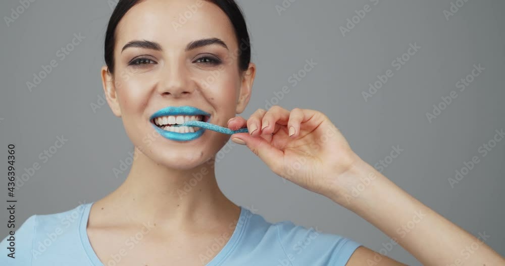 Beautiful young woman with unusual makeup eating sweet marmalade on grey background Beautiful young woman with unusual makeup eating sweet marmalade on grey background