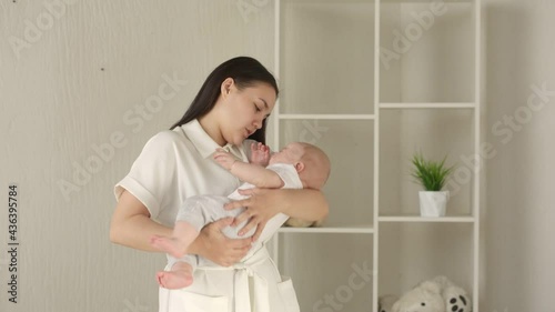 A young mother tries to calm her child by rocking in her arms. Lifestyle. Concept motherhood, first months of life, baby care