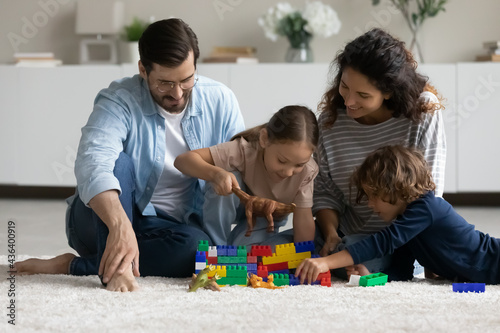 Happy multiethnic young family with small biracial children have fun play with toys blocks together on weekend. Smiling multiracial parents with ethnic kids engaged in playful game activity together.