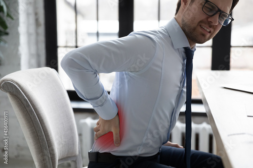 Unhappy office worker suffering from back pain attack due to overwork, muscle inflammation, chronic kidney disease. Manager trying to stand up, feeling backache, holding lumbar. Sedentary work concept photo