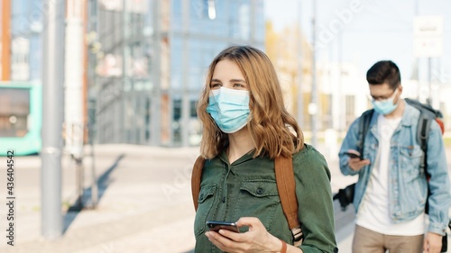 Portrait of Caucasian travelers in masks on street passing health control showing vaccination digital passport on smartphone man scan QR code vaccine certificate on cellphone and measuring temperature © VAKSMANV