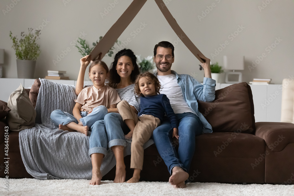 Portrait of smiling young multiethnic family with little kids relax at home hold paper roof excited move to new house together. Happy parents renters with children relocate. Rent, rental concept. Portrait of smiling young multiethnic family with little kids relax at home hold paper roof excited move to new house together. Happy parents renters with children relocate. Rent, rental concept.