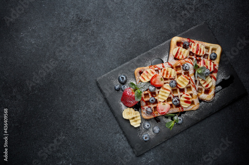 Tasty waffles with berries, mint, sweet sauce on slate serving board on grey background. Top view with copy space. Sweet meal. Dessert