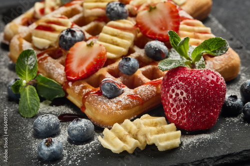 Tasty waffles with berries, mint and sweet sauce on slate serving board on grey background. Sweet meal. Dessert