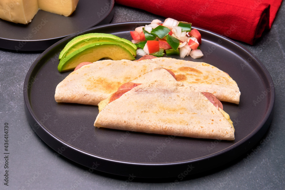 ham and cheese quesadillas served with avocado slices and pico de gallo sauce on a black plate. in horizontal view ham and cheese quesadillas served with avocado slices and pico de gallo sauce on a black plate. in horizontal view