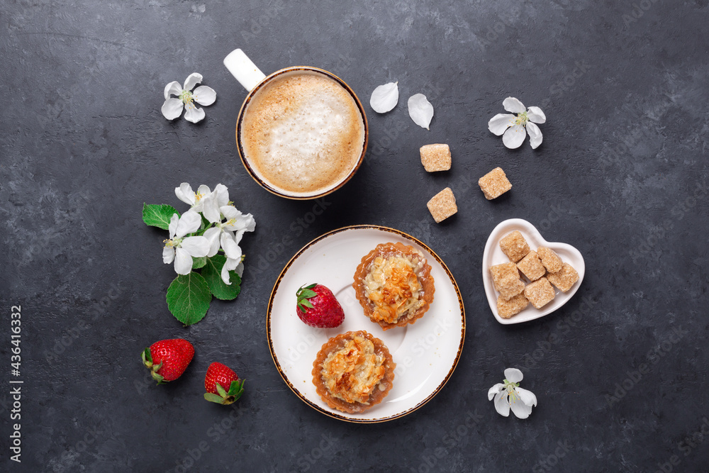 Cup of coffee with cakes and spring flowers on dark stone background. Top view Cup of coffee with cakes and spring flowers on dark stone background. Top view
