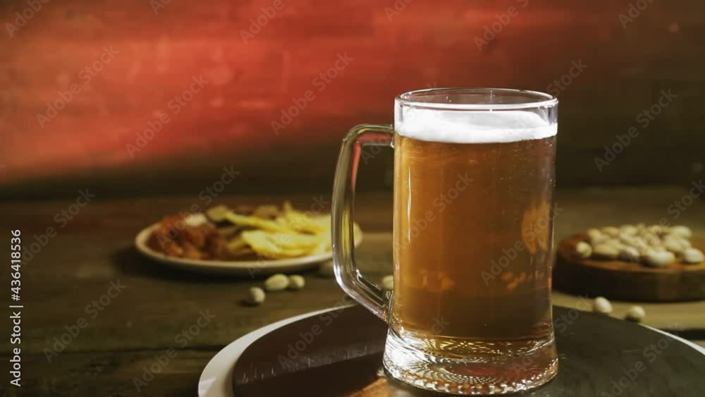 Foaming cold light beer in a glass mug on a wooden table with a snack rotates in a circle Foaming cold light beer in a glass mug on a wooden table with a snack rotates in a circle