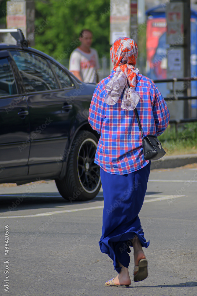 A woman in a headscarf crosses the street on a sunny day