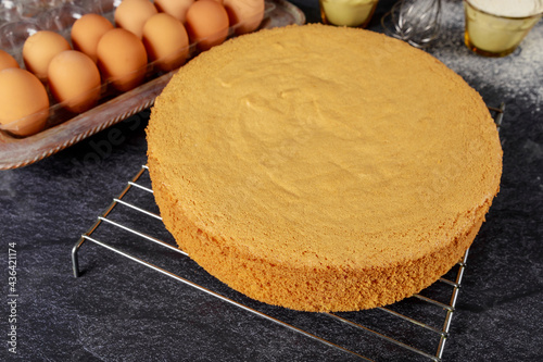 Homemade sponge cake on black background with eggs, flour and whisk. Bakery concept. photo