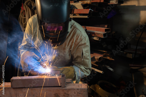 A welder is welding steel in an industrial factory. The welder wears protective clothing to work in the workplace.