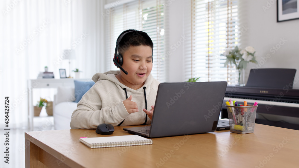 Young asia boy student wear headset headphone with computer laptop videocall talk present online e-learning class study with teacher, social distance learn language at home, homeschooling concept. Young asia boy student wear headset headphone with computer laptop videocall talk present online e-learning class study with teacher, social distance learn language at home, homeschooling concept.
