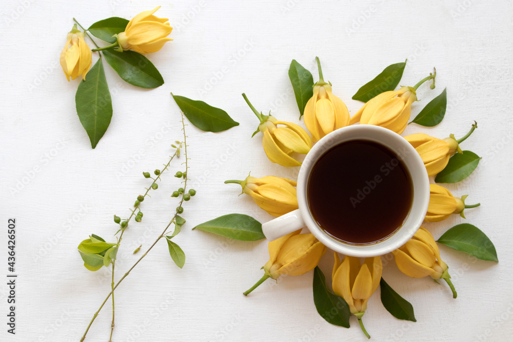 hot coffee espresso with yellow flowers ylang ylang, arrangement flat lay postcard style on background white wooden