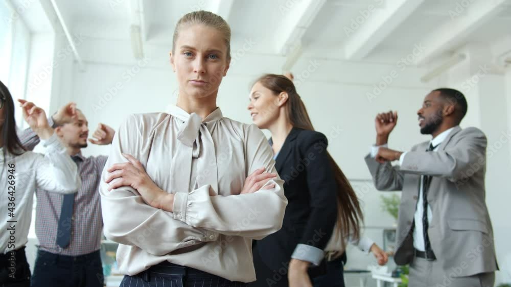 Business owner is standing in office with serious face while employees are dancing at corporate party relaxing having fun together. People and emotions concept.