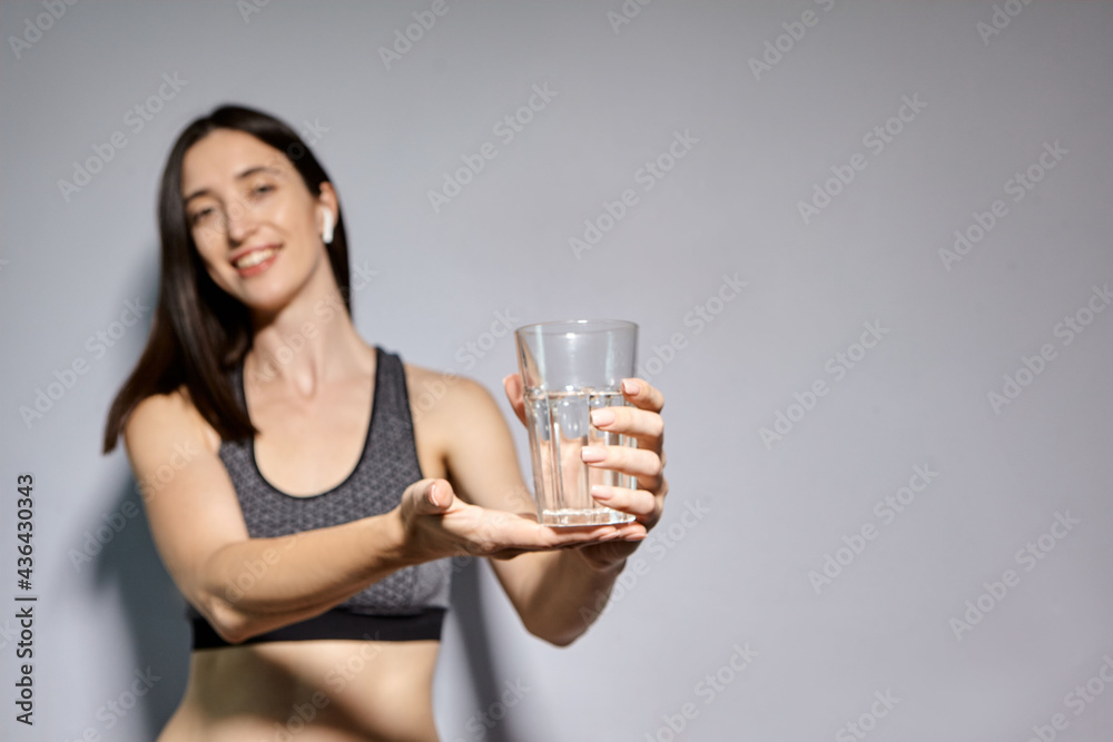 A woman in sports clothes and with wireless headphones drinks water. the concept of a healthy lifestyle and sports activities