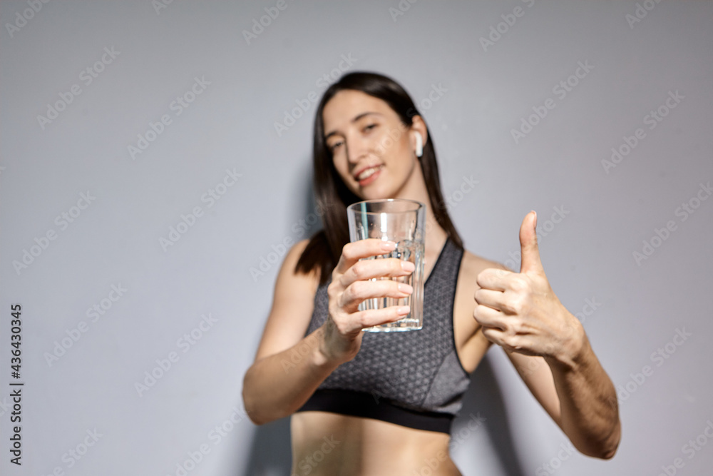 A woman in sports clothes and with wireless headphones drinks water. the concept of a healthy lifestyle and sports activities A woman in sports clothes and with wireless headphones drinks water. the concept of a healthy lifestyle and sports activities