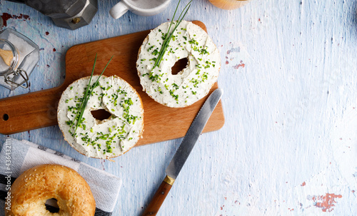 Breakfast table with bagels fresh cheese. Bagels with fresh cheese and herbs on a breakfast table , with fresh orange juice and coffee on the side.