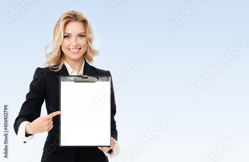 Portrait of young businesswoman showing blank clipboard, with copyspace area for text or slogan, on blue background. Success in business, job and education concept.