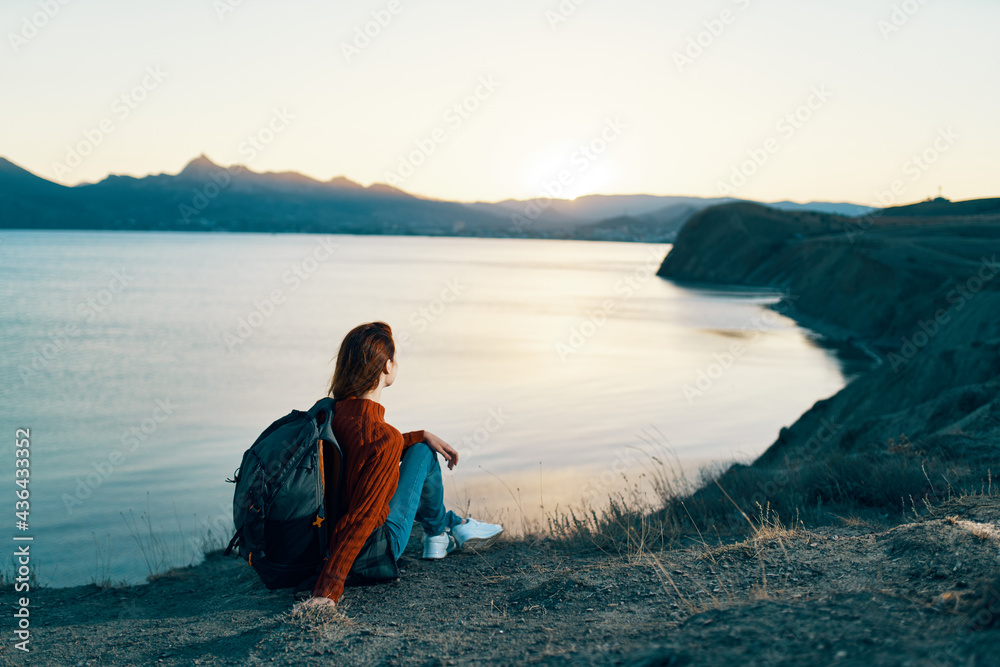 woman hiker with backpack in the mountains at sunset near the sea