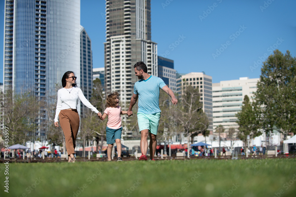 Happy family with little child son holding hands walking in city.