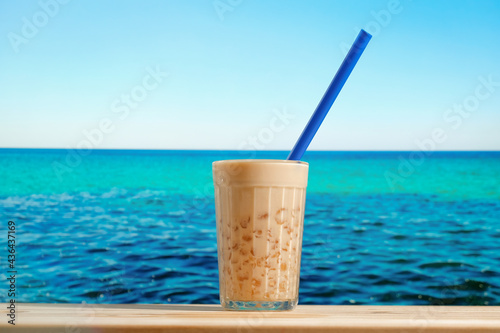 Glass of cold bubble tea. Summer beach bar concept. Milk boba tea with tapioca pearls, blue sea on background. 