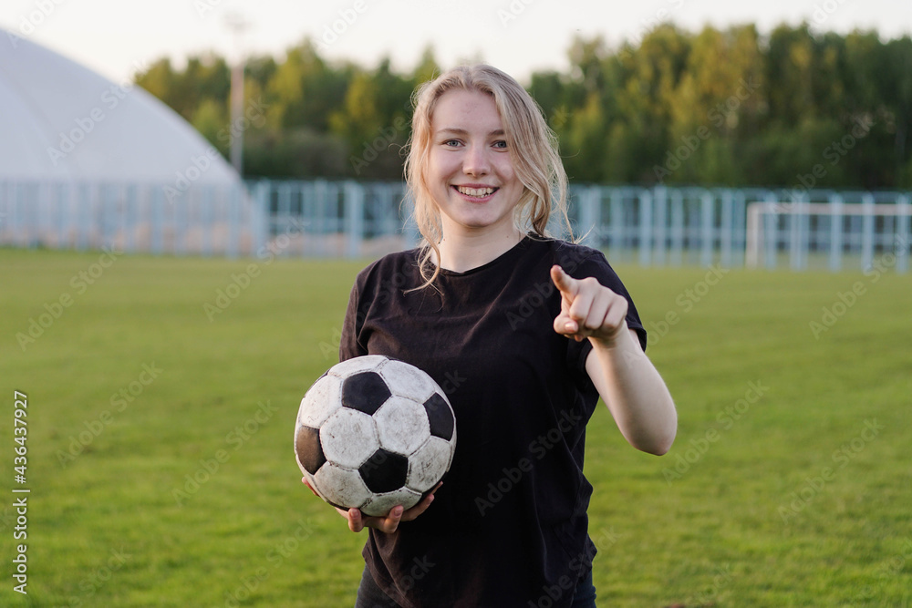 Young teen girl football player holding soccer ball pointing with finger to the camera and to you