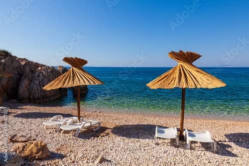 Girl relaxing on the deck chair while reading a book under a straw umbrella in the Oprna beach, Krk island