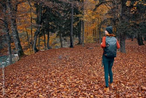 woman with backpack hiking travel in autumn park tall trees river fallen leaves © SHOTPRIME STUDIO