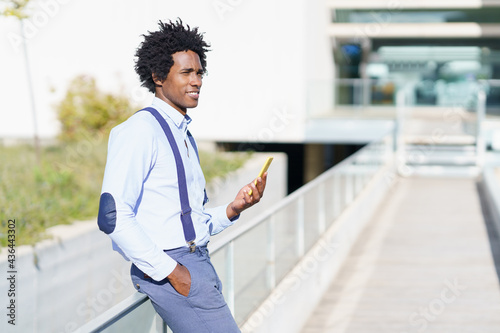 Black man with afro hairstyle using a smartphone near an office building.