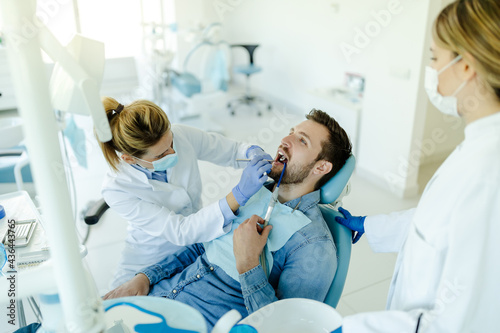 Man is sitting in dental chair at medical center while professional doctor fixing his teeth.