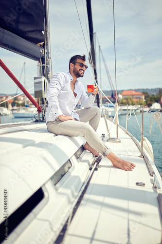 A young man sitting on a yacht and enjoying a coffe and a view on the dock. Summer, sea, vacation