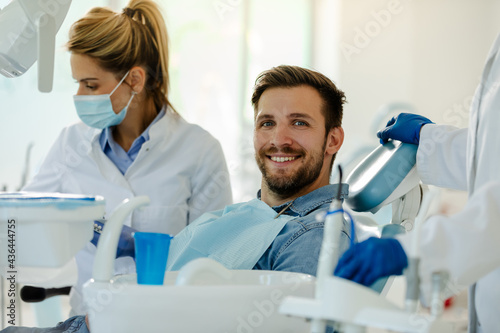 Happy young man sitting in dental chair, posing before examination and looking at the camera.