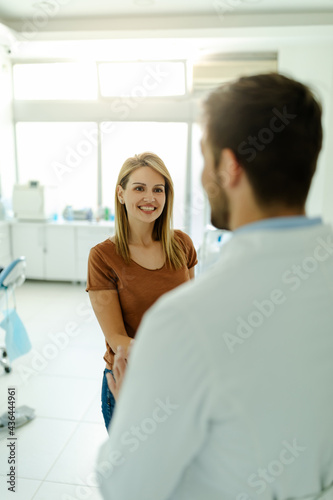 Male dentist and patient are shaking hands in a dental office after a successful dental treatment.