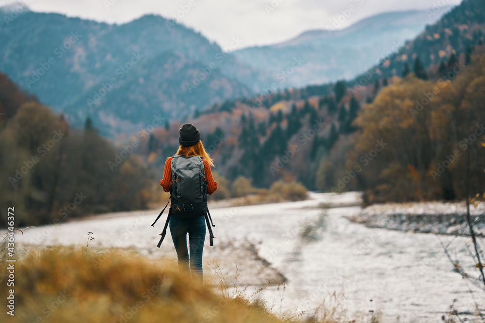 woman traveler with a backpack and in a hat near the river in the mountains in autumn