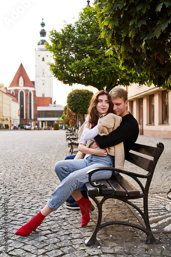Obraz na płótnie Beautiful young couple cuddling on a bench in a European town. Romatnic date and love concept. w salonie