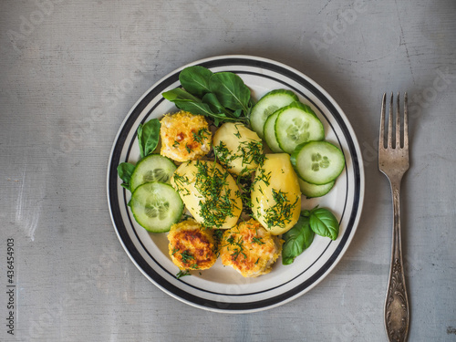 Boiled potatoes with fish cakes and herbs, fresh cucumber on a light plate,