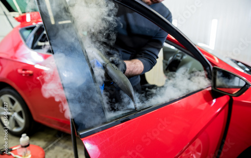 Car service worker cleans interiror with steam cleaner