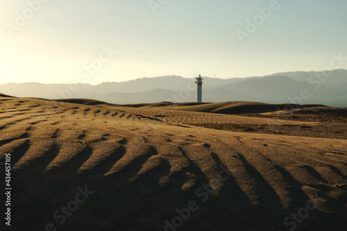 sunset at the lighthouse with the dunes of the delta del ebro natural park, punta del fangar, tarragona, catalonia, spain photo