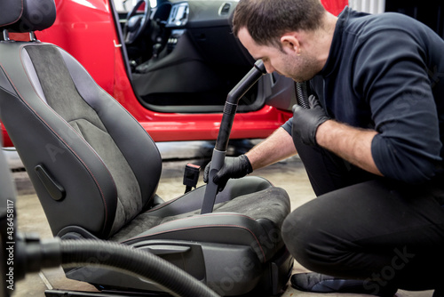 Car service worker cleaning car seat with vacuum cleaner.