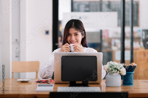 Charming asian businesswoman looking at camera and working with laptop computer in office